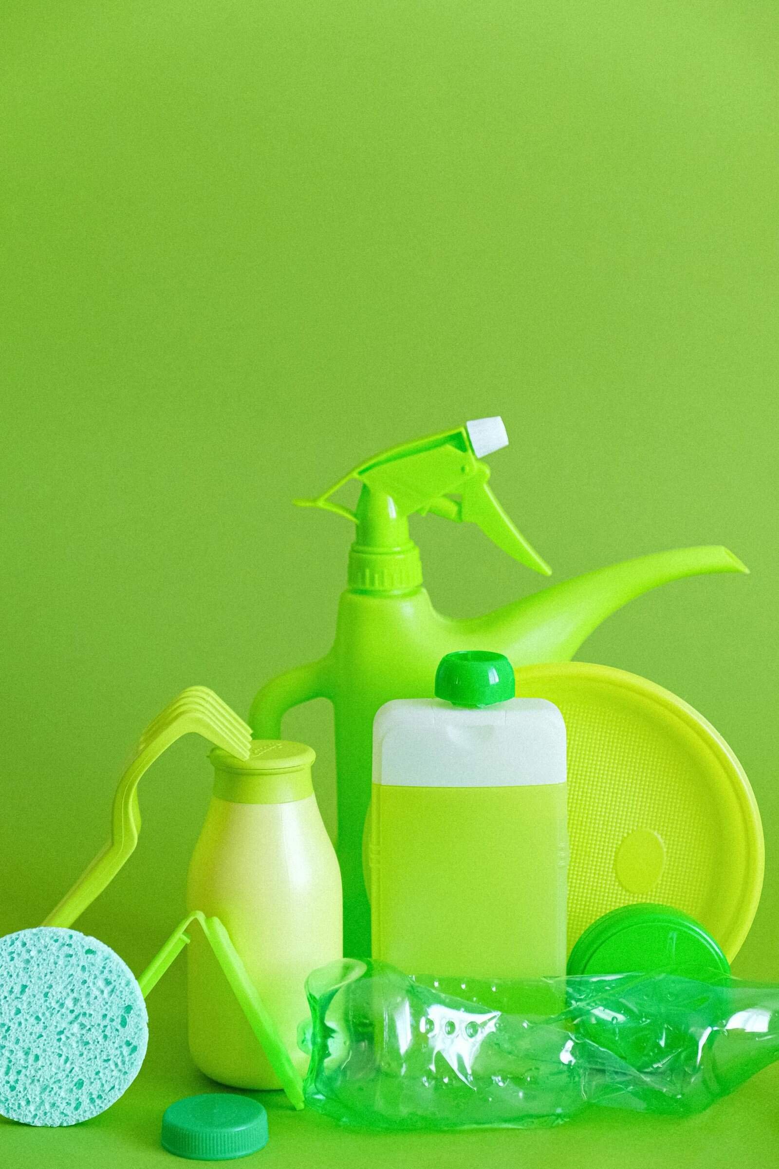 Assorted green cleaning supplies against vibrant green backdrop, promoting eco-friendly sanitation.