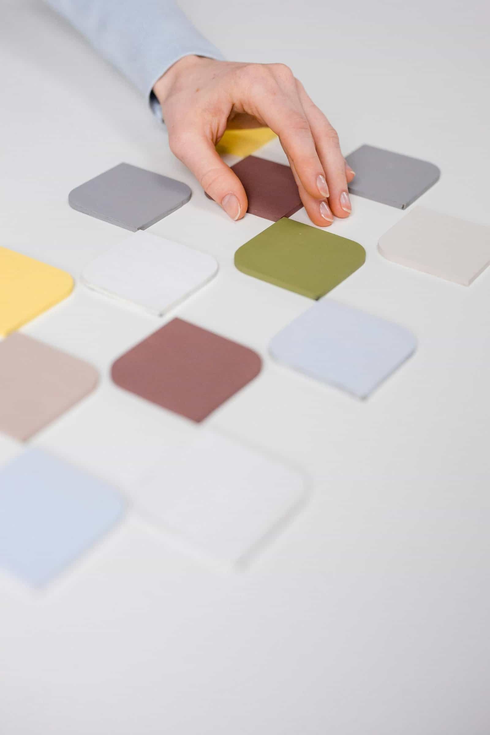 Close-up of a hand arranging diverse color swatches on a white table.