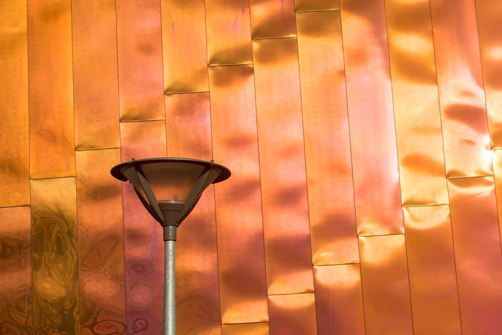 Close-up of a reflective copper facade with a streetlight, highlighting modern architecture.