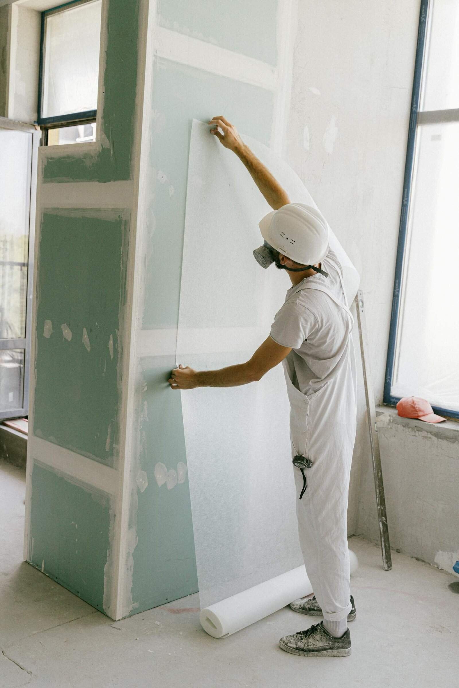 Construction worker in hard hat applying wallpaper inside a building under renovation.