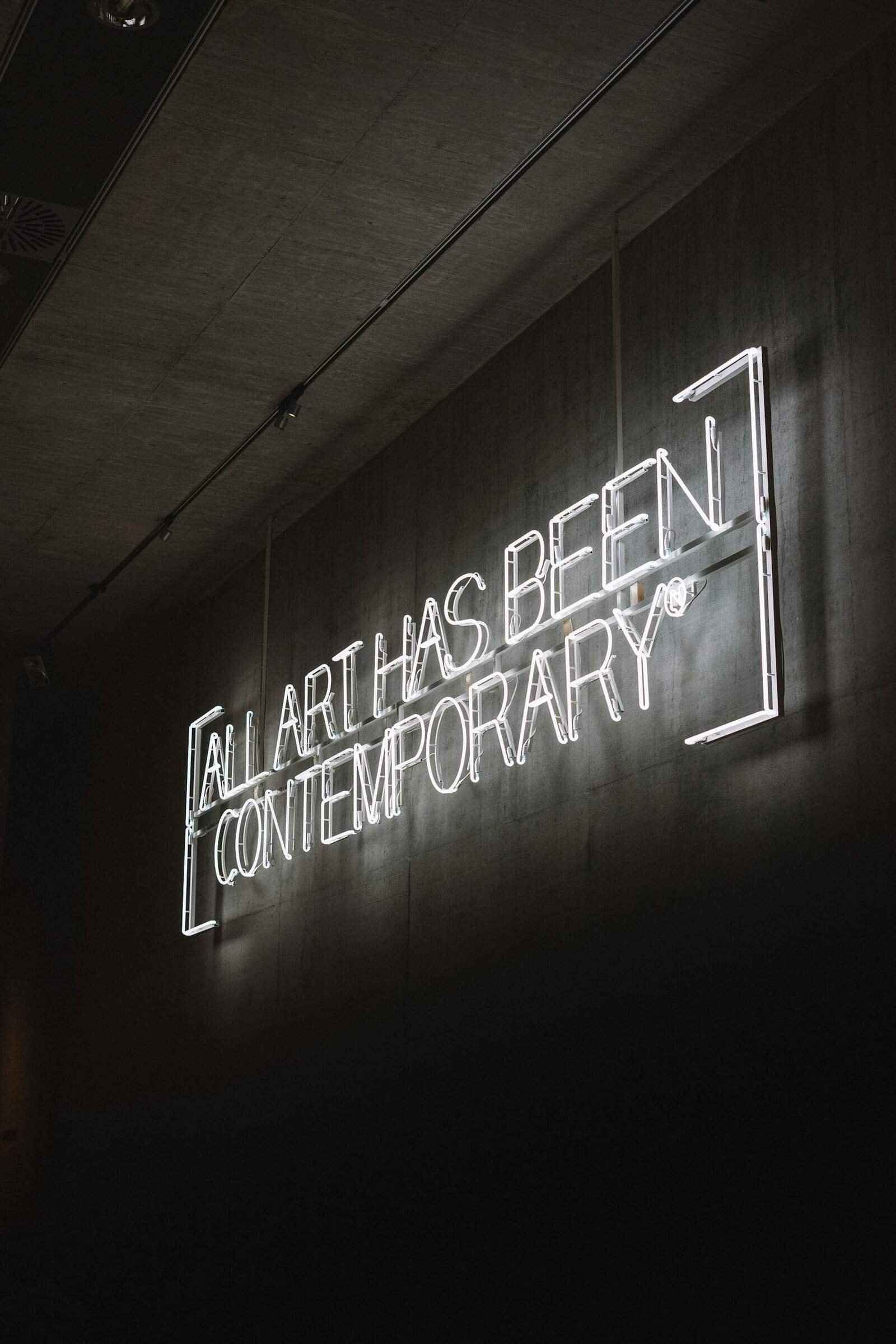 Illuminated neon sign stating 'All Art Has Been Contemporary' against a dark wall.